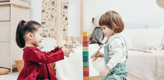 Boy sitting on the floor beside girl playing with blocks