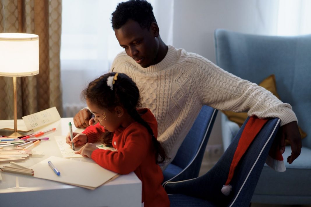 Dad watching his daughter write on paper