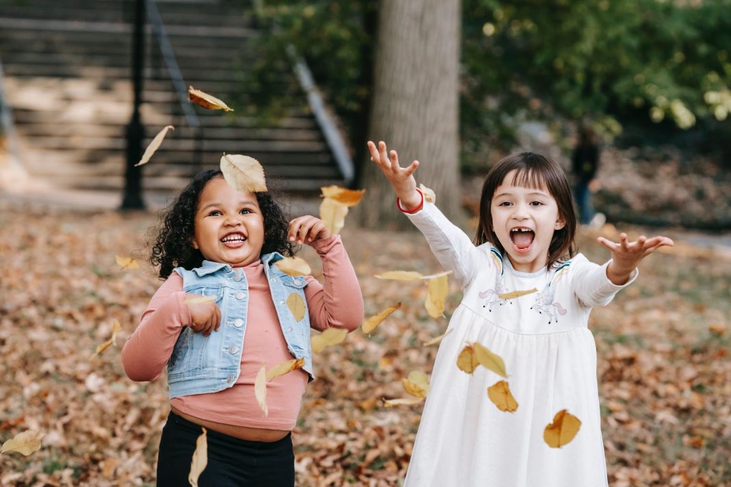 Two happy girls throwing foliage in the park