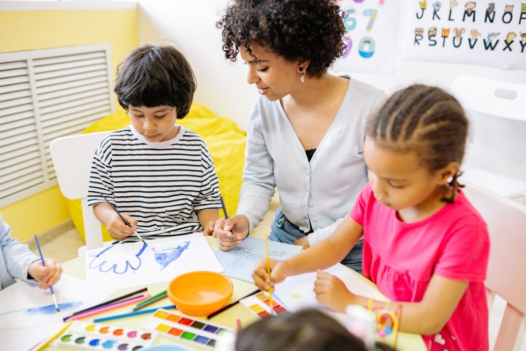 Children painting alongwith their teacher