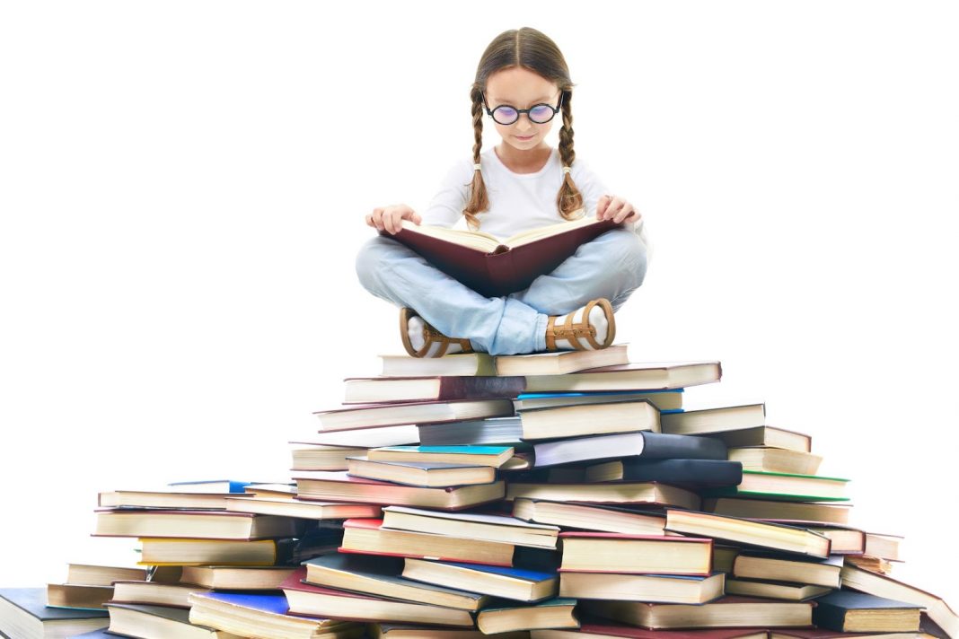 Kid sitting on a pile of books and reading