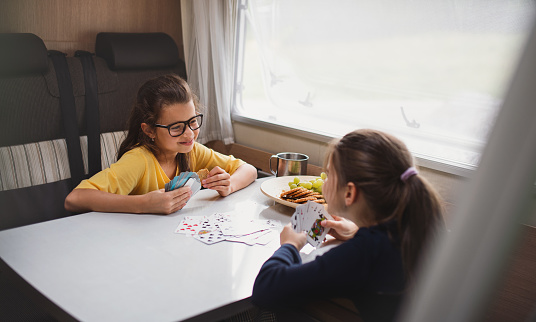 Happy small girls playing cards indoors in caravan family holiday trip